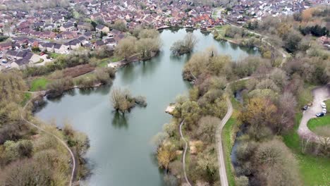 Drones-fly-over-ponds-and-trees-overlooking-a-pond-and-a-small-village