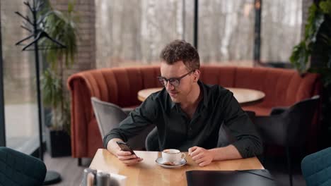 Cute-curly-man-in-a-cafe-spends-time-on-a-smartphone