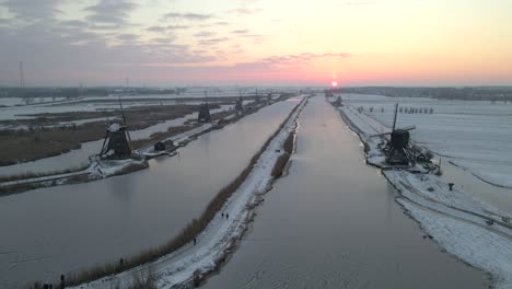 Colorful-sunrise-at-snowy-landscape-with-historic-Dutch-windmills,-aerial