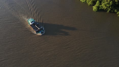 Aerial-top-down-showing-old-cargo-ship-transporting-wood-trunks-on-amazon-river-during-sunlight