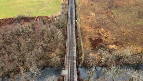 Aerial,-top-down-drone-video-footage-of-a-train-bridge-viaduct-running-over-a-valley-and-stream-in-the-Appalachain-Mountains-during-early-spring-on-a-cloud-day