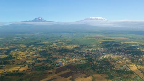 Paisaje-De-Kenia-Con-Un-Pueblo,-Kilimanjaro-Y-Parque-Nacional-Amboseli---Seguimiento,-Vista-Aérea-De-Drones