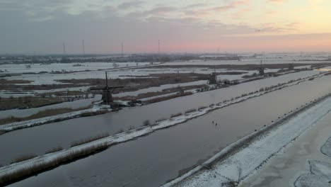 Sunrise-at-Dutch-Kinderdijk-Windmills-with-couple-ice-skating,-Travel-Europe