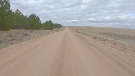Point-of-view-driving-on-a-straight-stretch-of-gravel-road-in-rural-Nebraska-on-a-cloudy-winter-day