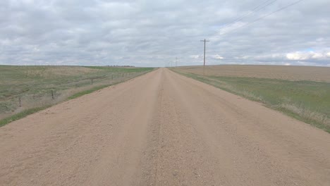 Punto-De-Vista-Mientras-Conduce-En-Un-Tramo-Recto-De-Camino-De-Ripio-A-Través-De-La-Zona-Rural-De-Nebraska-En-Un-Día-Nublado-A-Principios-De-La-Primavera