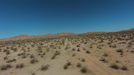 Riding-a-four-wheeler-in-the-Mojave-Desert's-rugged-landscape-as-viewed-from-a-first-person-drone
