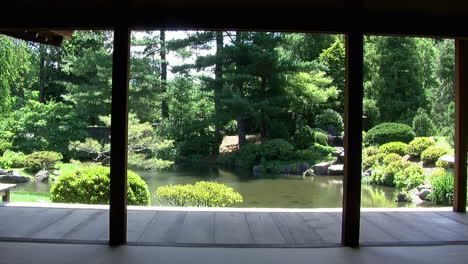 Vista-Del-Jardín-Japonés-Y-Del-Estanque-Desde-El-Interior-De-Una-Casa-Japonesa-Con-Las-Paredes-Retiradas