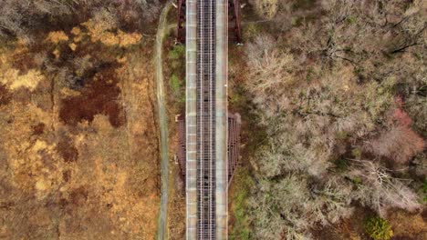 Aerial,-top-down-drone-video-footage-of-a-train-bridge-viaduct-running-over-a-valley-and-stream-in-the-Appalachain-Mountains-during-early-spring-on-a-cloud-day
