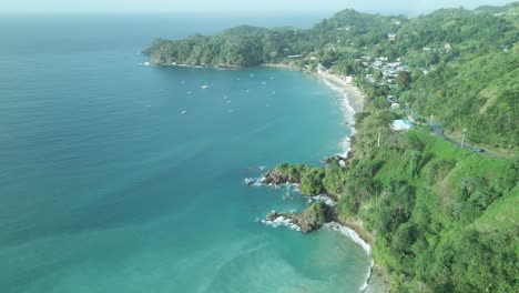 Aerial-view-of-Castara-Bay-nestled-on-the-hillside-with-rainforest-as-a-backdrop,-and-the-ocean-below
