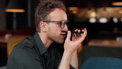 Stylish-curly-man-with-glasses-sitting-in-a-cafe-talking-on-the-phone