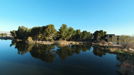 Flying-over-a-pond-oasis-in-the-Mojave-Desert-with-the-trees-and-sky-reflecting-off-the-water