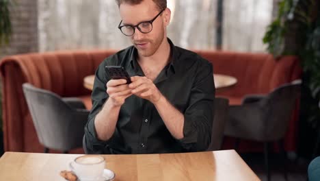 close-up-portrait-of-a-handsome-young-man-in-a-cafe-spends-time-with-a-smile-in-his-smartphone