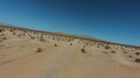 Four-wheeler-driving-along-a-dusty-trail-in-the-Mojave-Desert-on-a-hot-day---aerial-first-person-view