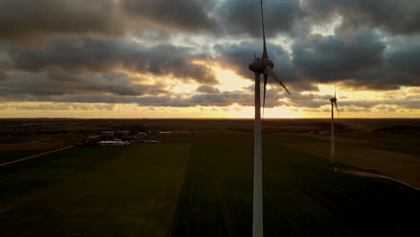 Aerial-view-showing-silhouette-of-rotating-windmills-in-front-of-cloudy-sunset-in-backdrop