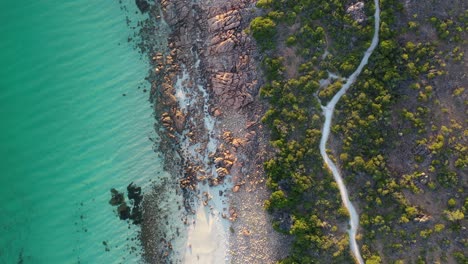 Top-down-aerial-view-of-exotic-tropical-Castle-Rock-beach-and-coastal-road-between-trees-on-golden-hour-sunlight