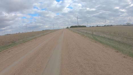 Point-of-view-driving-on-a-straight-stretch-of-graveled-road,-past-harvested-fields