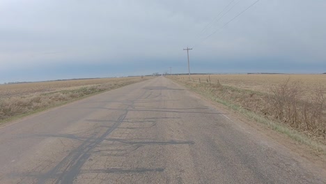 Vista-De-La-Ventana-Trasera-Mientras-Conduce-Por-Una-Antigua-Carretera-Asfaltada-Entre-Campos-Cosechados-En-La-Zona-Rural-Del-Centro-Sur-De-Nebraska-En-Un-Día-Nublado-De-Invierno