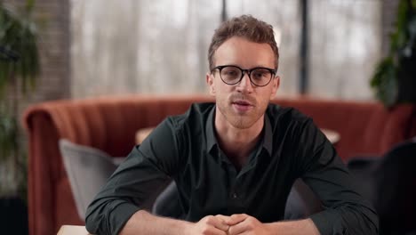 Handsome-curly-man-with-glasses-talks-looking-into-the-camera