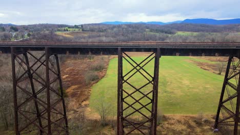 Luftdrohnenvideoaufnahmen-Eines-Eisenbahnbrückenviadukts,-Das-Im-Frühen-Frühling-An-Einem-Wolkentag-über-Ein-Tal-In-Den-Appalachain-Bergen-Führt,-Umgeben-Von-Bergen-Und-Ackerland