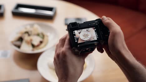 Close-up-of-male-hands-holding-a-mirrorless-camera-and-taking-pictures-of-food-on-the-table
