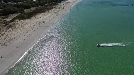 Aerial-view,-water-scooter-approaching-to-white-sand-beach-on-scenic-australian-coastline-on-sunny-day,-orbit-drone-shot