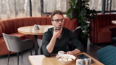 Handsome-man-in-a-cafe-talking-in-a-voice-chat-via-smartphone