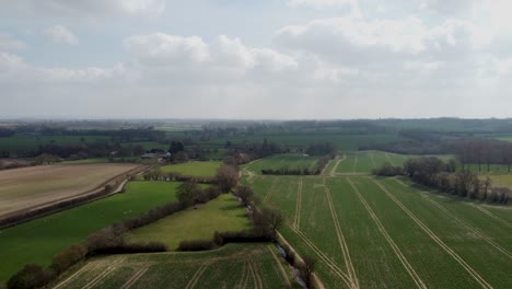 Aerial-view-over-green-fields-with-light-cloudy-sky