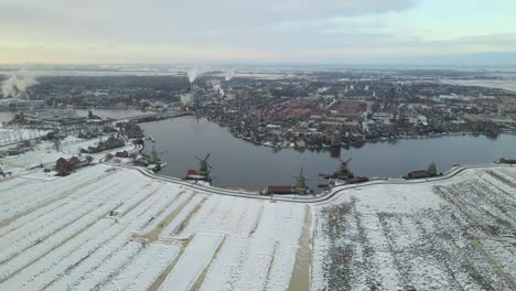 Snow-covered-farmland-with-Dutch-windmills-and-city-of-Zaandijk,-aerial