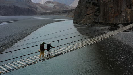 Pakistani-Women-Crossing-The-Hussaini-Suspension-Bridge-Above-Hunza-River-In-Hunza,-Gilgit-Baltistan,-Pakistan