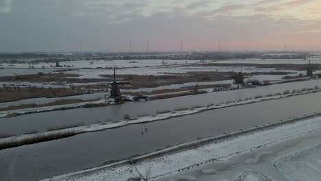 Tranquil-morning-at-traditional-windmills-in-Netherlands,-couple-ice-skating