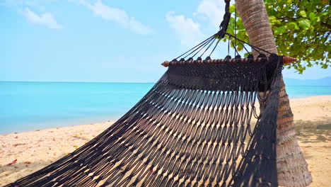Empty-hammock-on-deserted-sandy-tropical-beach,-close-up-of-swinging-bed-by-blue-sea-on-exotic-travel-destination,-full-frame
