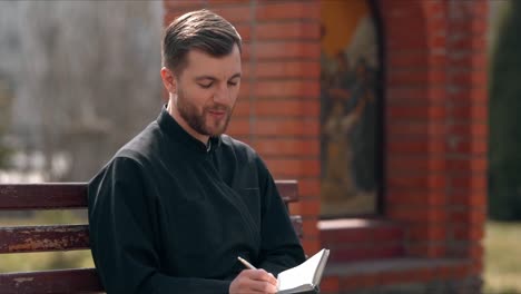 A-cute-smiling-priest-writes-down-his-thoughts-in-a-notebook