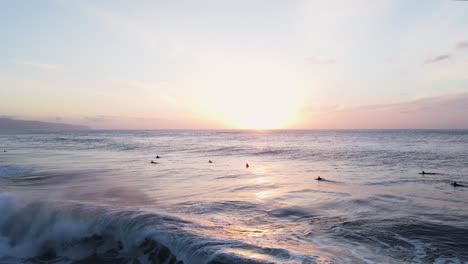 Surfers-at-sunset,-O'ahu-North-Shore-Hawaii-Pacific-Ocean,-4K-aerial-view