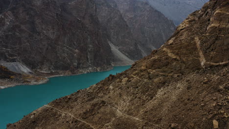 Drone-shot-revealing-Attabad-lake-behind-rocky-mountain-side,-Himalaya