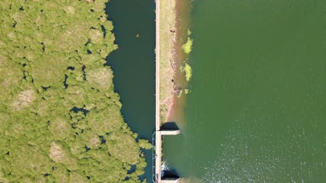 Bird's-eye-view-of-river-with-dam-and-bridge-while-kids-play-on-top-of-it-on-a-sunny-day