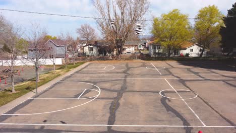 Slow-pan-drone-clip-sideways-to-the-right-of-tennis-shoes-trainers-on-phone-wire-and-a-small-and-empty-distressed-basketball-court-after-covid-19-lockdowns-end