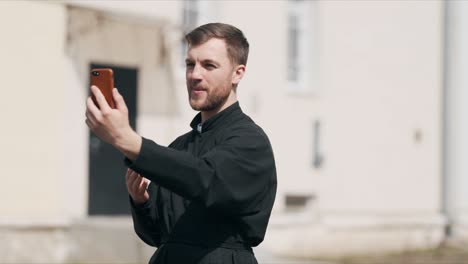 A-young-pleasant-priest-is-talking-on-a-video-call-via-a-smartphone