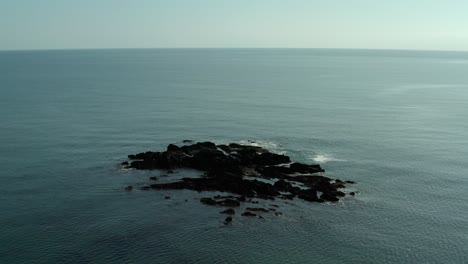 Aerial-wide-angle-orbit-of-rocks-on-ocean-water-on-calm-day