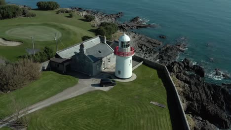 Aerial-spinning-shot-of-lighthouse-near-low-tide-ocean-on-sunny-day