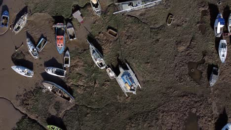 Various-stranded-abandoned-fishing-boat-wreck-shipyard-in-marsh-mud-low-tide-coastline-aerial-birds-eye-view