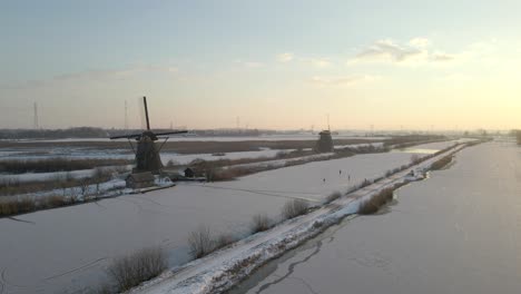 Malerischer-Sonnenschein-An-Traditionellen-Holländischen-Windmühlen-Im-Winter,-Menschen-Beim-Eislaufen