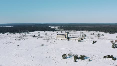 Aerial:-Ice-covered-Veluwe-National-Park-with-Radio-Kootwijk-building,-tracking-pan-shot