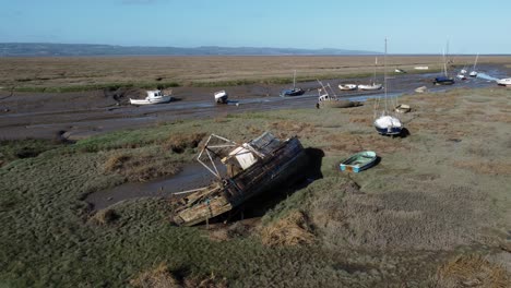 Stranded-abandoned-fishing-boat-wreck-shipyard-in-marsh-mud-low-tide-coastline-aerial-view-orbit-right