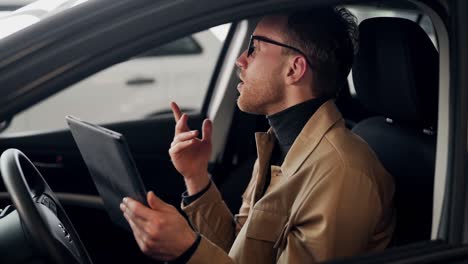 Stylish-young-man-talking-in-the-car-on-video-via-tablet