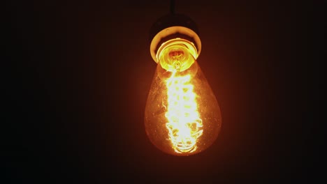 Squirrel-cage-incandescent-light-bulb-hanging-in-the-dark