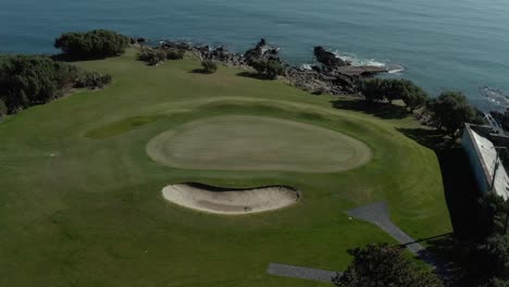 Aerial-birds-eye-view-of-golf-course-by-the-calm-ocean-at-day,-no-people