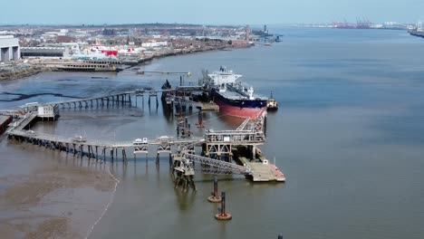 Crude-oil-tanker-ship-loading-at-refinery-harbour-terminal-aerial-view-high-pull-back