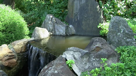 El-Agua-Se-Derrama-Sobre-El-Borde-De-Una-Cascada-Ornamental-En-Un-Jardín-Japonés