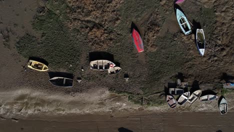 Various-stranded-abandoned-fishing-boat-shipyard-in-marsh-mud-low-tide-coastline-aerial-birds-eye-view