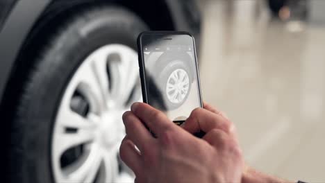 Close-up-of-male-hands-taking-pictures-with-smartphone-of-new-wheel-in-car